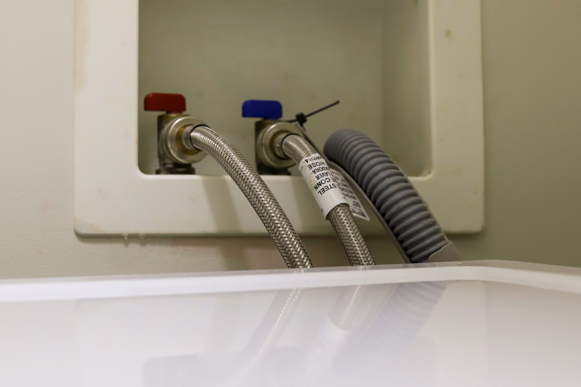 Washing machine hoses connected to hot and cold taps in a laundry cupboard setup