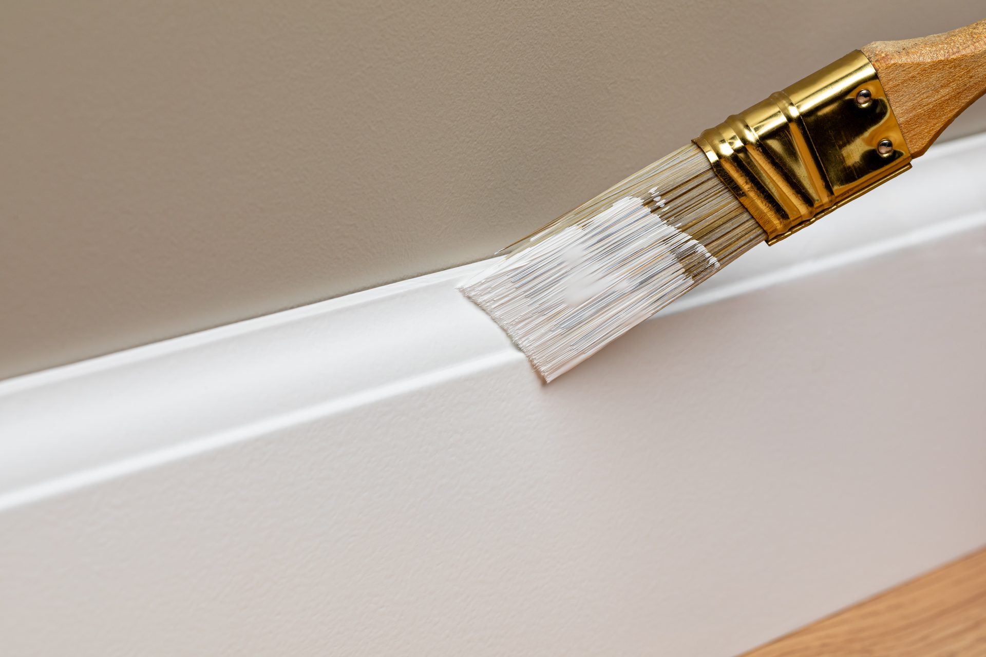 Paintbrush applying white oil-based enamel to a timber skirting board